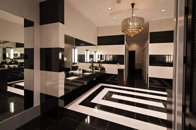 Guest bathroom with black and white marble tile, black granite countertops, a tiered chandelier, and a geometric floor pattern.