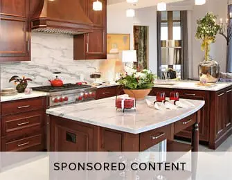 Luxury kitchen with dark wood cabinetry, marble countertops, and a large stainless steel range. Center island features a fruit bowl and red glassware.