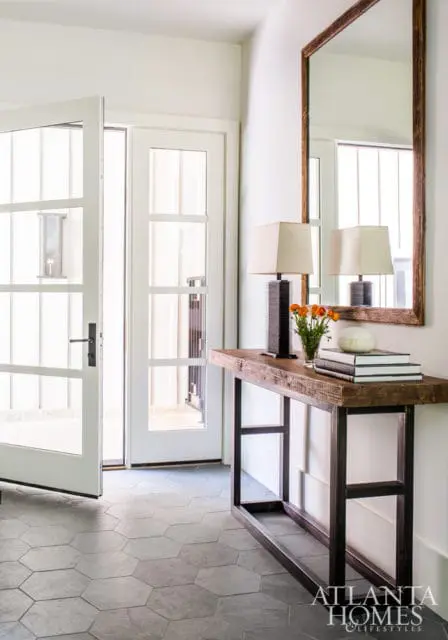 Entryway with white double doors, hexagonal gray tile floor, and a rustic wood console table with two lamps and a mirror