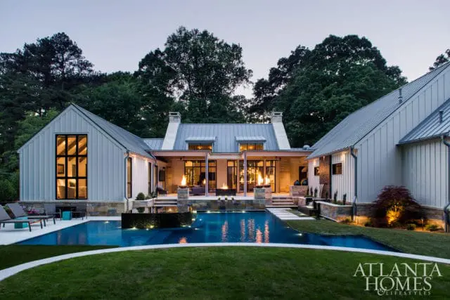 Modern farmhouse style home with white vertical siding, metal roof, and large windows overlooking a swimming pool and patio with fire features.