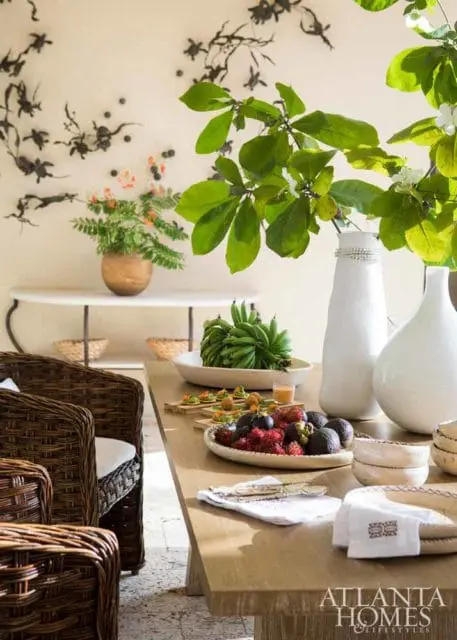 Dining table with woven chairs, fruit platters, and decorative wall art.