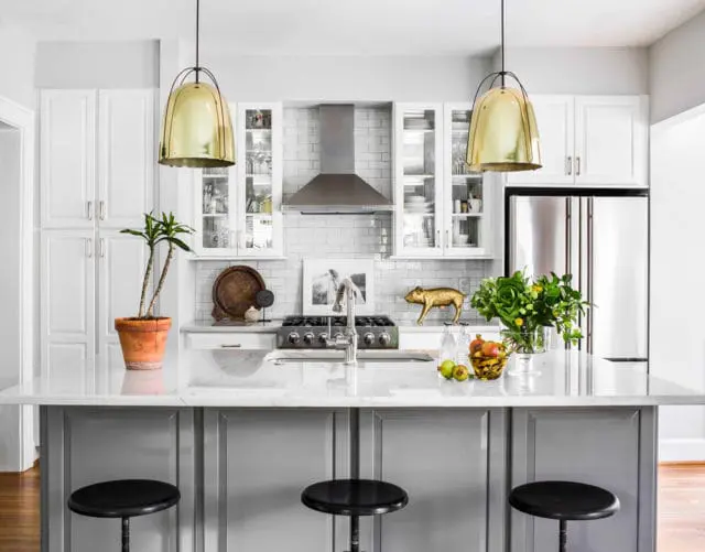 White kitchen with gray island, marble countertops, stainless steel appliances, and brass pendant lights.