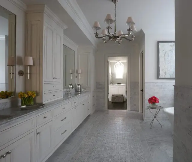 White bathroom with marble countertops, custom white cabinetry, mosaic tile flooring, and a doorway leading to another room with a window.