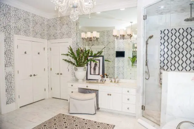 Modern bathroom with black and white polka dot wallpaper, white double doors, marble vanity with gold fixtures, and a glass-enclosed shower with geometric tile accent.