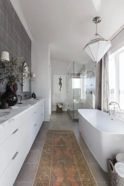 Modern bathroom with white double vanity, marble countertops, gray patterned tile backsplash, freestanding soaking tub, and glass-enclosed shower with marble walls.