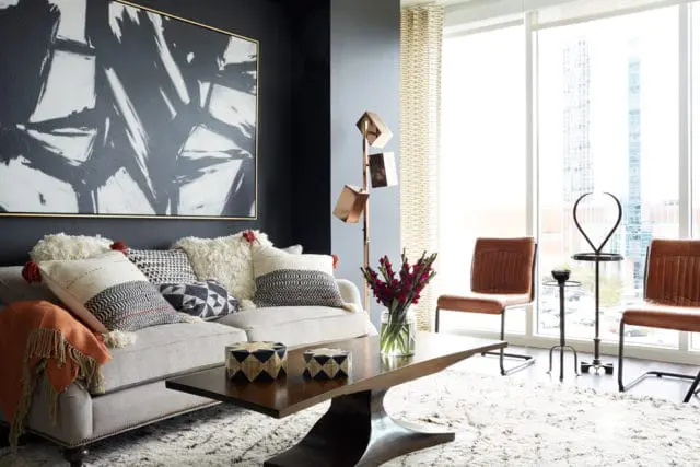 Living room with a light gray sofa, black and white abstract art, patterned throw pillows, a dark wood coffee table, and two brown leather chairs by a large window.