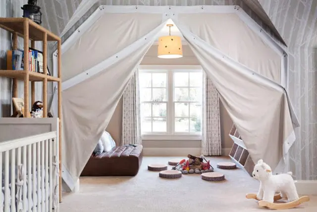 Children's bedroom with a tent-like canopy, faux campfire, leather ottoman, rocking lamb, and a crib.