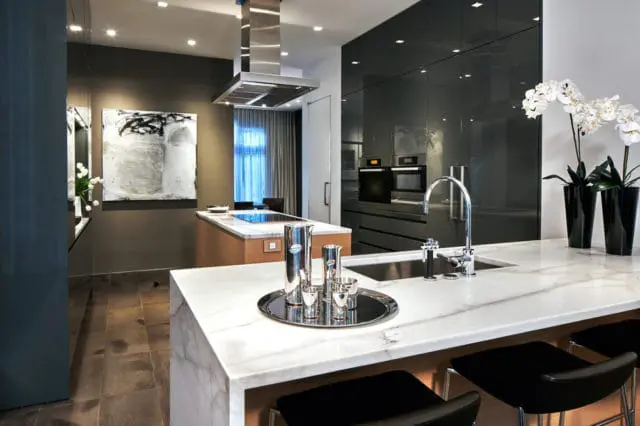 Modern kitchen with white marble island, stainless steel range hood, dark grey cabinetry, and abstract art on the wall.