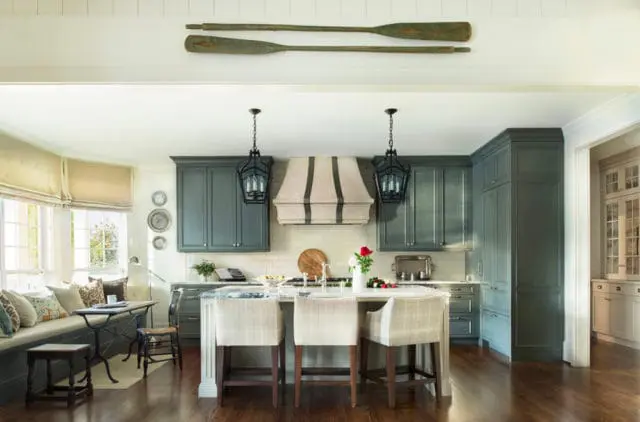 Gray kitchen with white subway tile backsplash, a striped range hood, and a white island with plaid bar stools. Two antique oars hang above the cabinets.