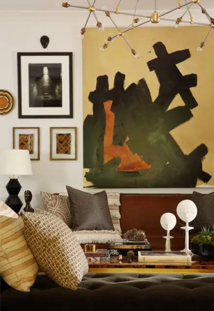 Living room with abstract art, patterned pillows, a black lamp, and a modern chandelier.