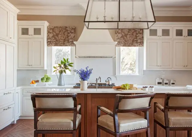 Kitchen with white cabinetry, marble countertops, and a wood island featuring upholstered bar stools. A large pendant light hangs above.