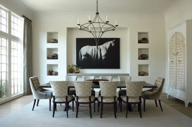 Dining room with a dark wood table surrounded by upholstered chairs, a large black and white horse artwork above a recessed shelf, and tall windows with grey curtains.