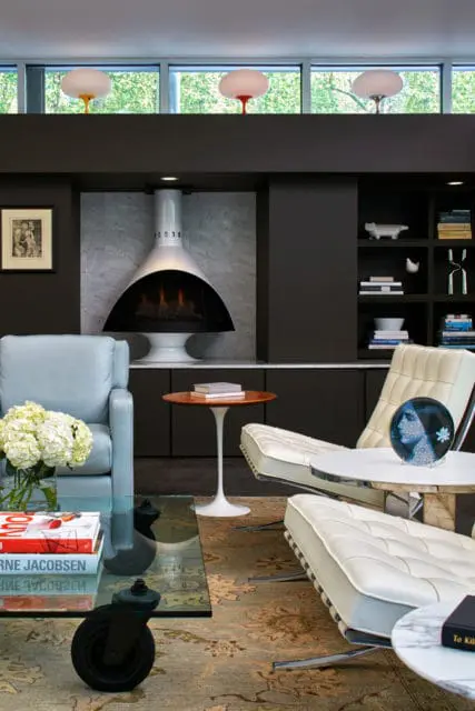 Living room with a white mid-century modern fireplace, light blue leather sofa, white leather lounge chairs, and a glass coffee table with books.