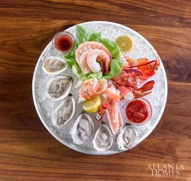 Seafood platter with oysters, shrimp, lobster, and crab legs served on ice with lemon wedges and cocktail sauce.