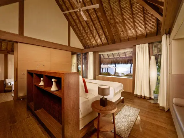 Bedroom with thatched roof, wooden beams, and ocean view.