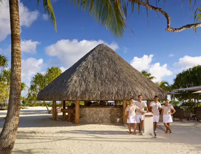 Staff at a thatched hut bar on a tropical beach.