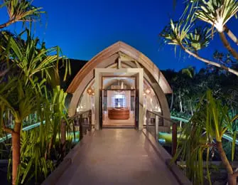 Mutineer resort entrance at dusk, featuring a wooden bridge and tropical foliage.