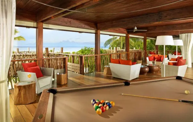 Wooden covered patio with seating, pool, and ocean view.