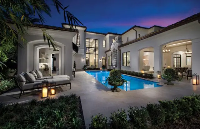 Modern Mediterranean style home exterior at dusk with a bright blue swimming pool, outdoor lounge furniture, and illuminated lanterns.