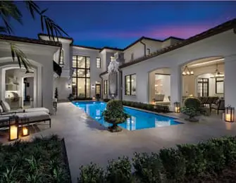 Modern white stucco home with a bright blue pool, large windows, and outdoor seating areas at dusk.