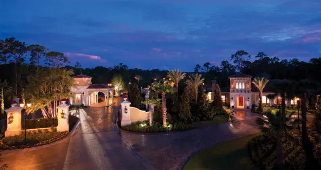 Italianate style villa entrance with arched loggia, stone accents, and palm trees at dusk.