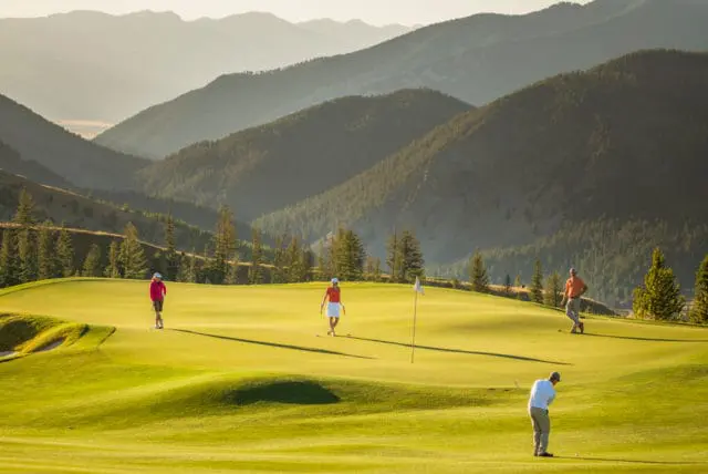 Golfers on a green course with rolling hills and mountains in the background during golden hour