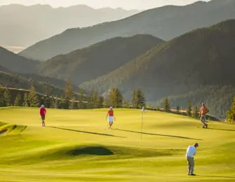 Golfers on a sunlit green with rolling hills and mountains in the background at Moonlight Basin