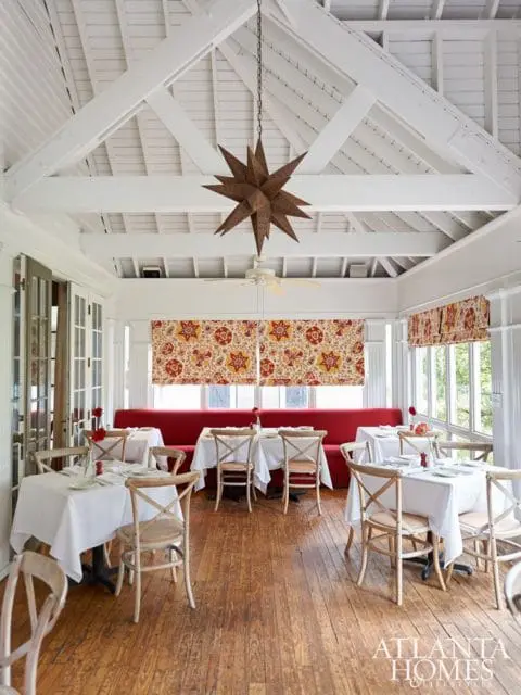 Dining room with white tables, cross-back chairs, red banquette seating, and a large metal star pendant light under a vaulted ceiling.