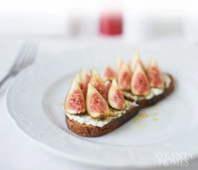 Two slices of toasted bread topped with ricotta cheese, sliced figs, and a drizzle of honey on a white plate with a fork to the left.