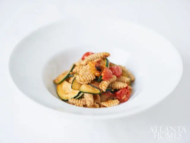 Pasta with zucchini and cherry tomatoes in a white bowl, with the Atlanta Homes & Lifestyles logo in the lower right corner.