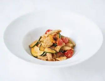 Garganelli pasta with zucchini, cherry tomatoes, and herbs in a white bowl