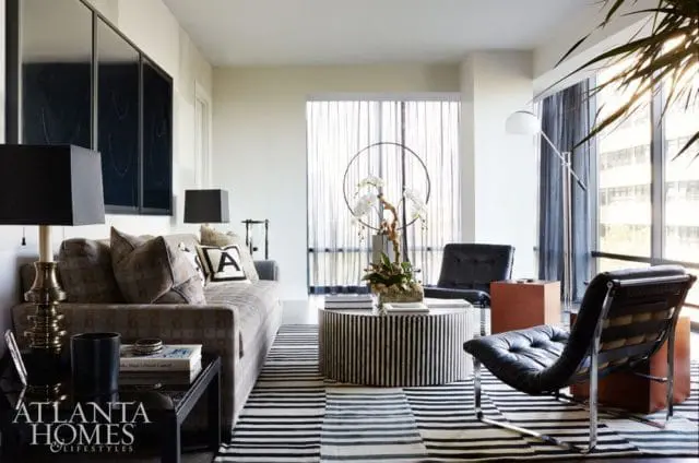 Living room with a patterned sofa, black leather chairs, a striped coffee table with orchids, and a black and white striped rug.