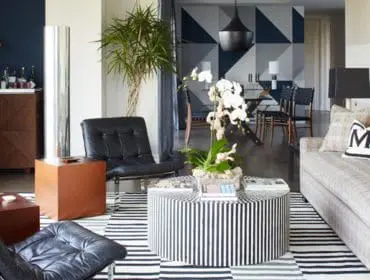 Living room with black leather armchairs, a striped ottoman, a patterned sofa with decorative pillows, and a geometric accent wall in navy and gray.