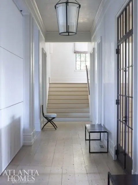 Hallway with white paneled walls, a large glass lantern pendant light, and a staircase leading to a landing with a window.