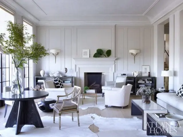Light-filled living room with white walls, fireplace, plush seating, and a large dark wood dining table with a tree in a glass vase.