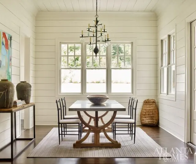 Dining room with shiplap walls, a marble-top dining table with a wooden base, upholstered chairs, and a large abstract painting on the wall.
