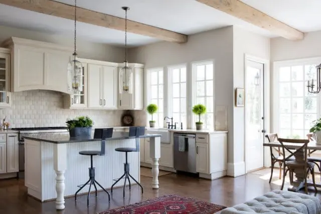 Cream kitchen with white subway tile backsplash, dark granite island with seating, pendant lights, and exposed wooden beams.