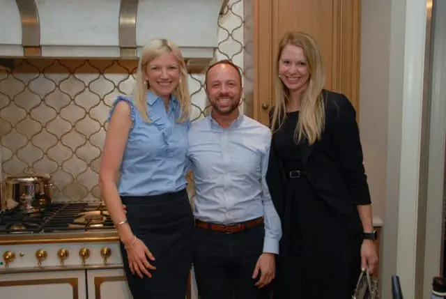Three people posing in a kitchen with a decorative tile backsplash and a professional-grade range.