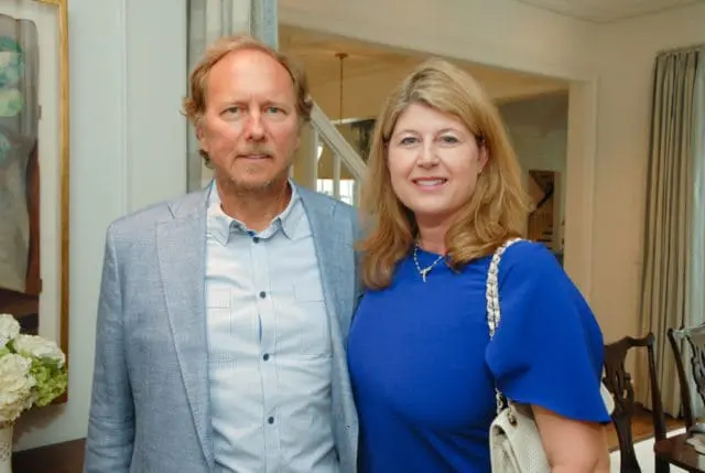 Man in a light blue suit jacket and striped shirt stands next to a woman in a royal blue dress, both smiling.