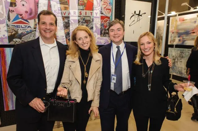 Four people pose for a photo in front of colorful artwork. The two men wear suits, and the two women wear dresses and jackets.