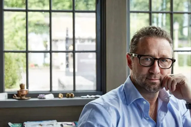 Man with short, graying hair and glasses wearing a blue striped button-down shirt, resting his chin on his hand.