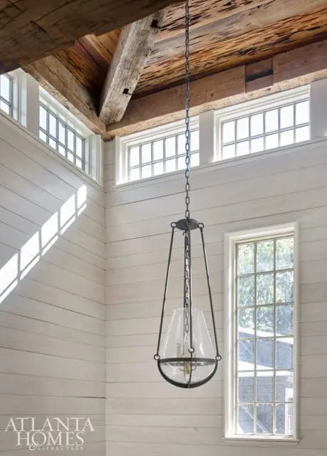 Interior with white shiplap walls, exposed wooden beams on the ceiling, and a large glass and metal pendant light fixture.