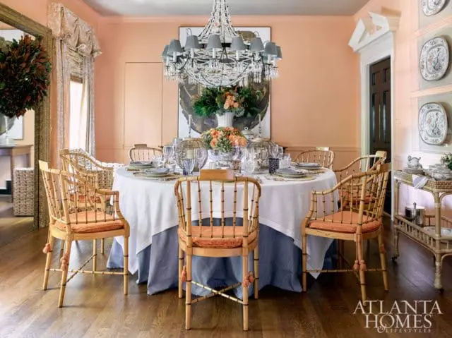 Peach dining room with a round table set for a meal, bamboo chairs with orange cushions, and a crystal chandelier.