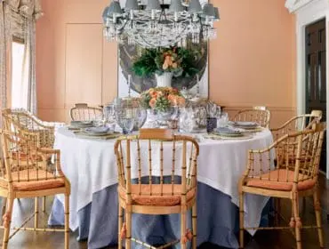 Peach dining room with a round table set for dinner, bamboo chairs with orange cushions, and a large crystal chandelier.