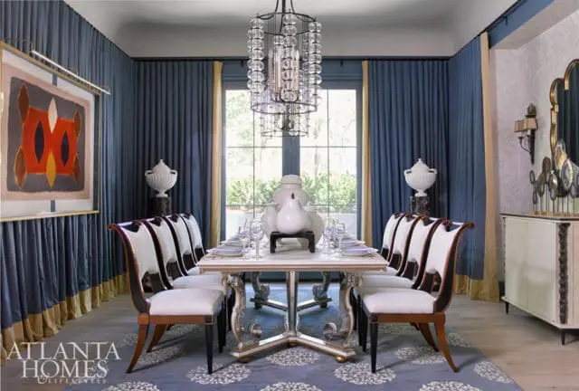 Formal dining room with blue drapes, a white and gold dining table set for a meal, and ornate chairs with white upholstery.