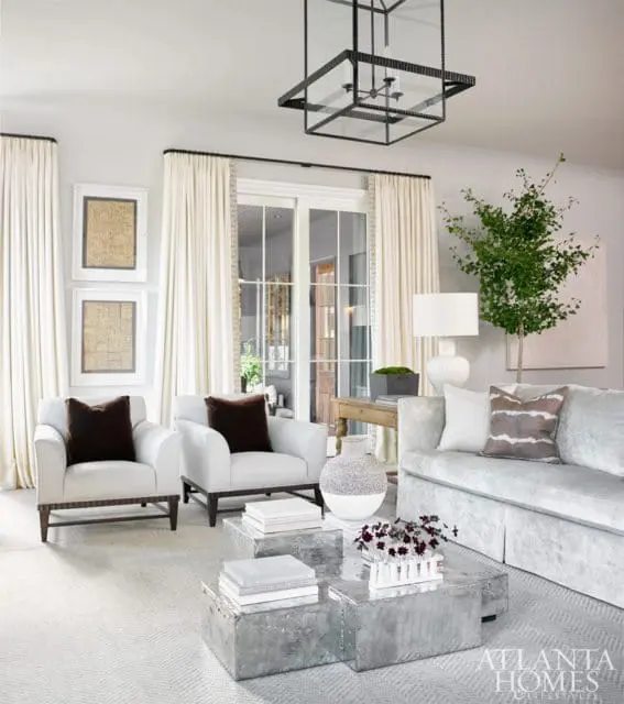 Living room with two white armchairs, a light blue sofa, metallic cube coffee tables, and a large black lantern chandelier.