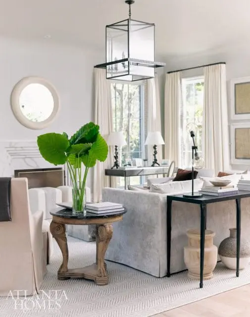 Living room with light gray sofa, cream upholstered chairs, round marble-top side table with carved wooden base, and a large glass lantern chandelier.