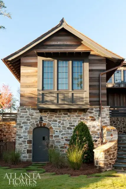 Stone foundation with a wooden upper level featuring a bay window and a dark arched door. Copper gutters and a stone staircase are visible.
