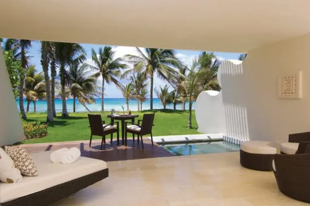 Terrace with lounge chairs, a small dining set, and a plunge pool overlooking a tropical beach with palm trees.