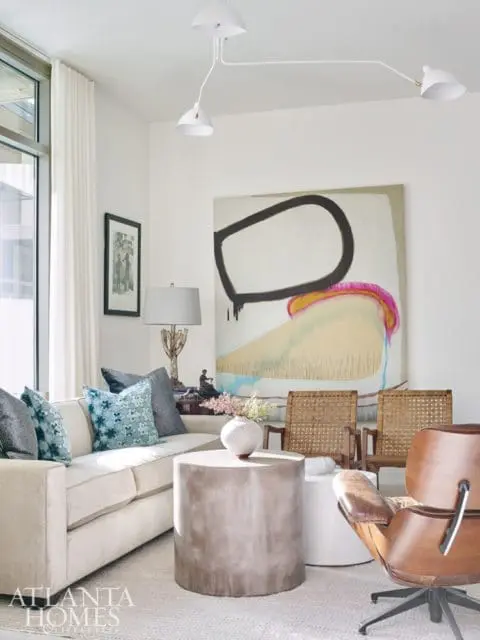 Living room with a cream sofa, abstract art, concrete coffee table, and leather Eames lounge chair.